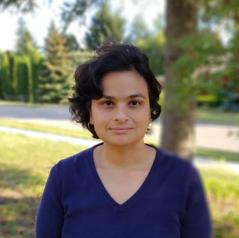 Photo of Dr. Ashirbani Saha wearing a dark blue shirt with tress behind her