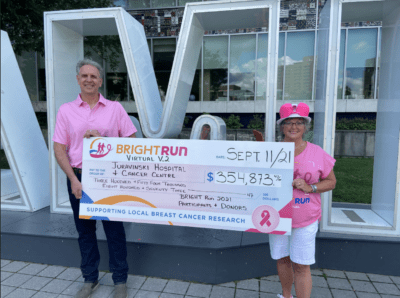 Man and woman wearing pink, holding a novelty cheque in the amount of $354,873
